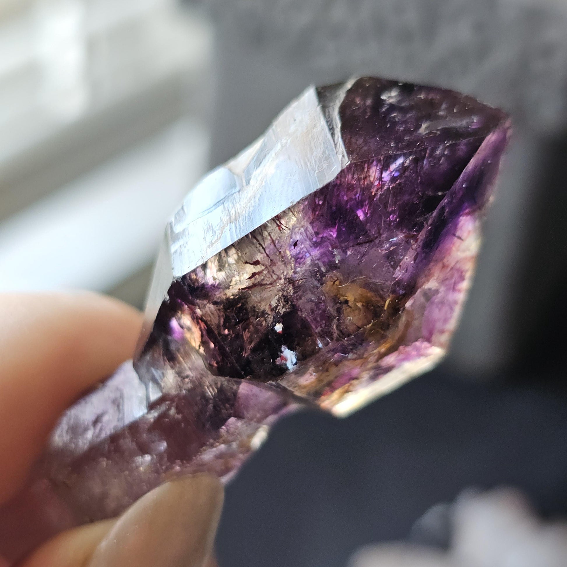 May include: A purple amethyst crystal with a clear, glassy point. The crystal has a golden brown inclusion and a few white spots.