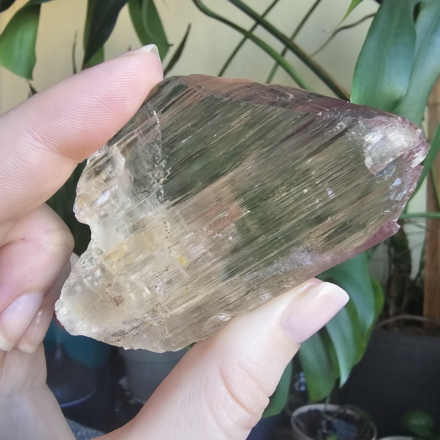 May include: A large, clear, faceted crystal with a light brown hue and a slight green tint. The crystal has a striated texture and is translucent. The crystal is shaped like a point and has a flat base.